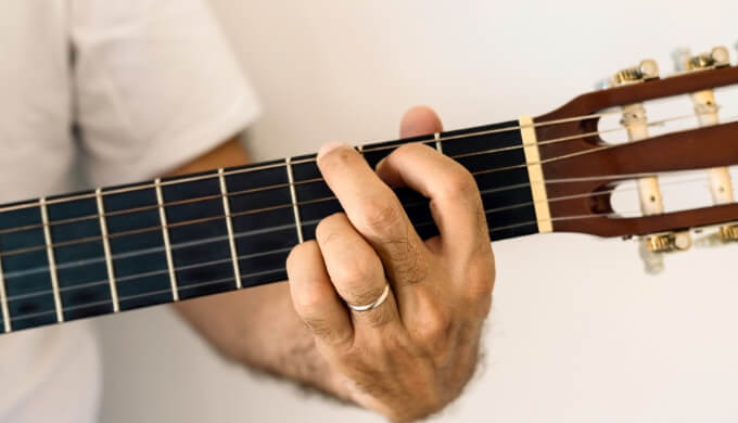 En mann holder et gitargrep på gripebrettet på en gitar.