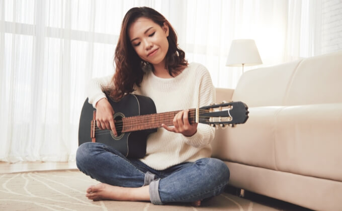 Kvinne som sitter på gulvet og spiller gitar.